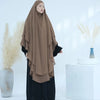 Eine Frau trägt einen beigen, zweilagigen Chiffon-Niqab und schwarze Kleidung vor weißem Hintergrund.