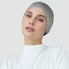 Eine Frau trägt eine graue Stretch-Baumwoll-Hijab-Underscarf-Kappe und ein weißes Rollkragen-Top.