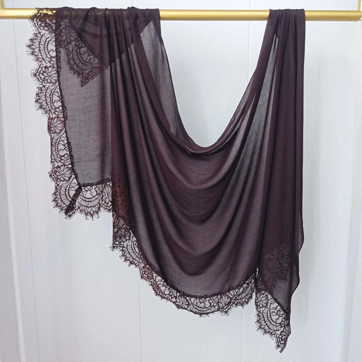 Hijab de encaje morado oscuro drapeado sobre un percha dorada.