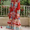 Una mujer vistiendo un colorido vestido maxi floral bohemio con flecos, de pie al aire libre frente a una barandilla blanca y