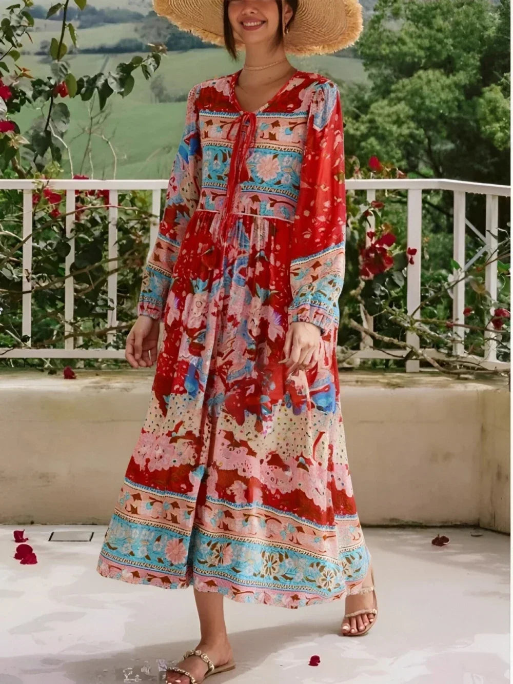 Una mujer vistiendo un colorido vestido maxi floral bohemio con flecos, de pie al aire libre frente a una barandilla blanca y