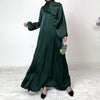 Modelo vistiendo un maxi vestido de satén verde esmeralda oscuro con hijab a juego y clutch de pedrería dorada.