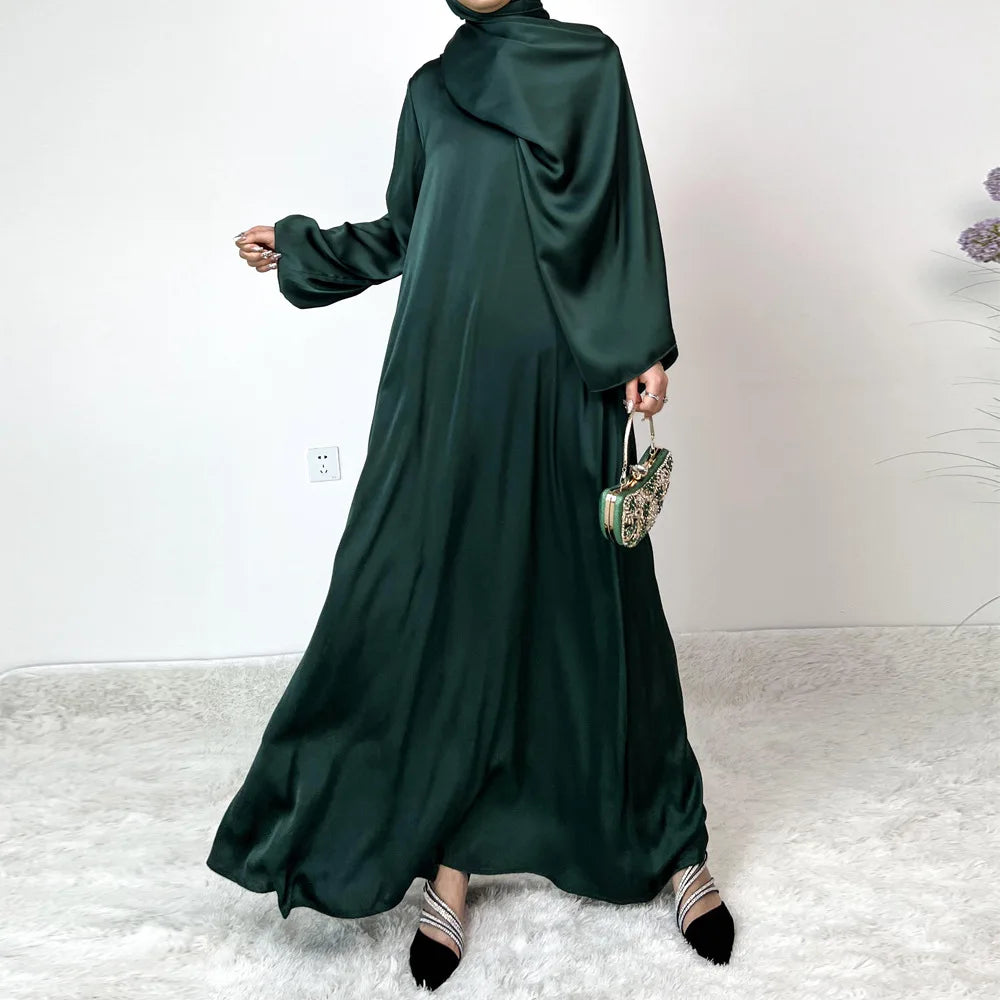 Modelo vistiendo un maxi vestido de satén verde esmeralda oscuro con hijab a juego y clutch de pedrería dorada.