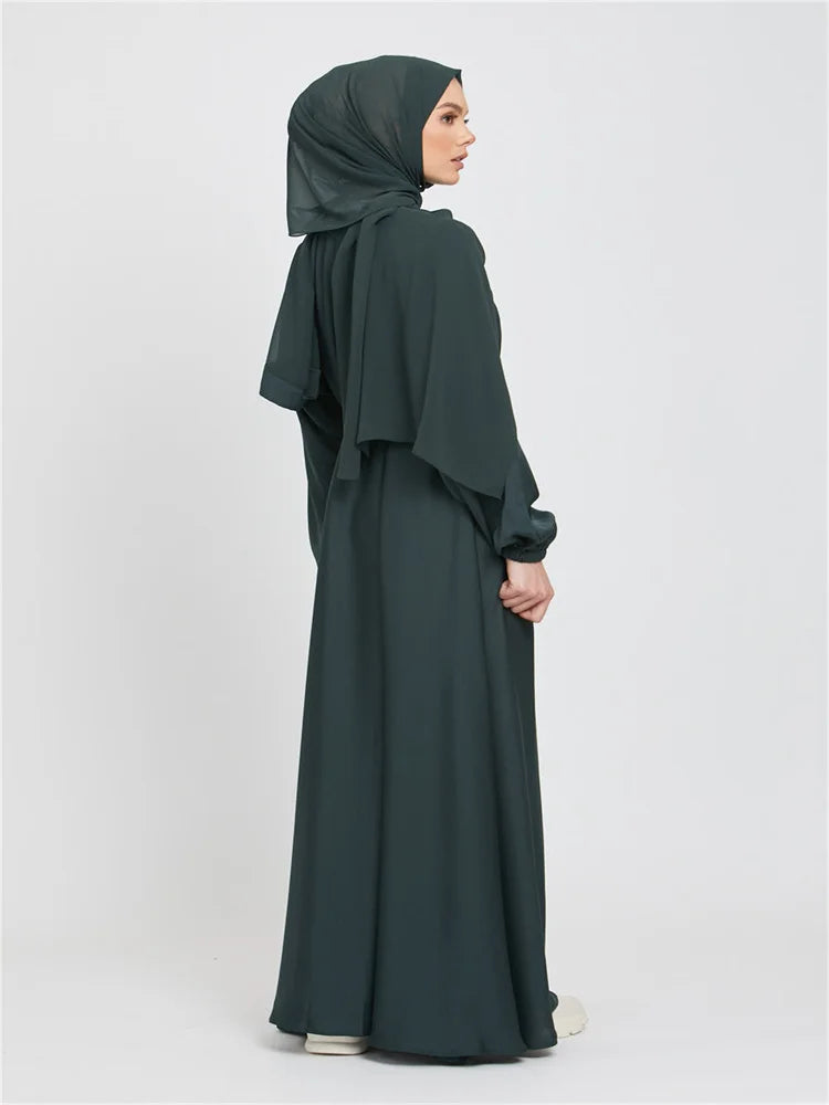Eine Frau in einem dunkeltürkisen marokkanischen Kaftan-Abaya mit einem drapierten Kopftuch.