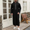 A man wearing a black Moroccan embroidered thobe jellaba standing in a doorway.