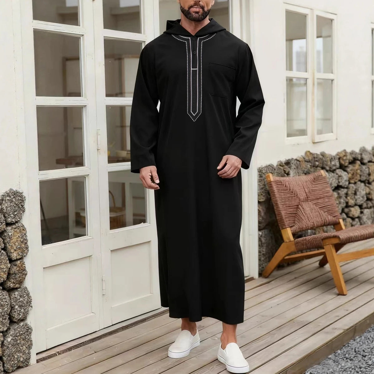 A man wearing a black Moroccan embroidered thobe jellaba standing in a doorway.