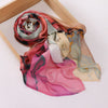 Foulard voile imprimé fluide rose, pêche et vert sourd drapé dans un cadre en bois.