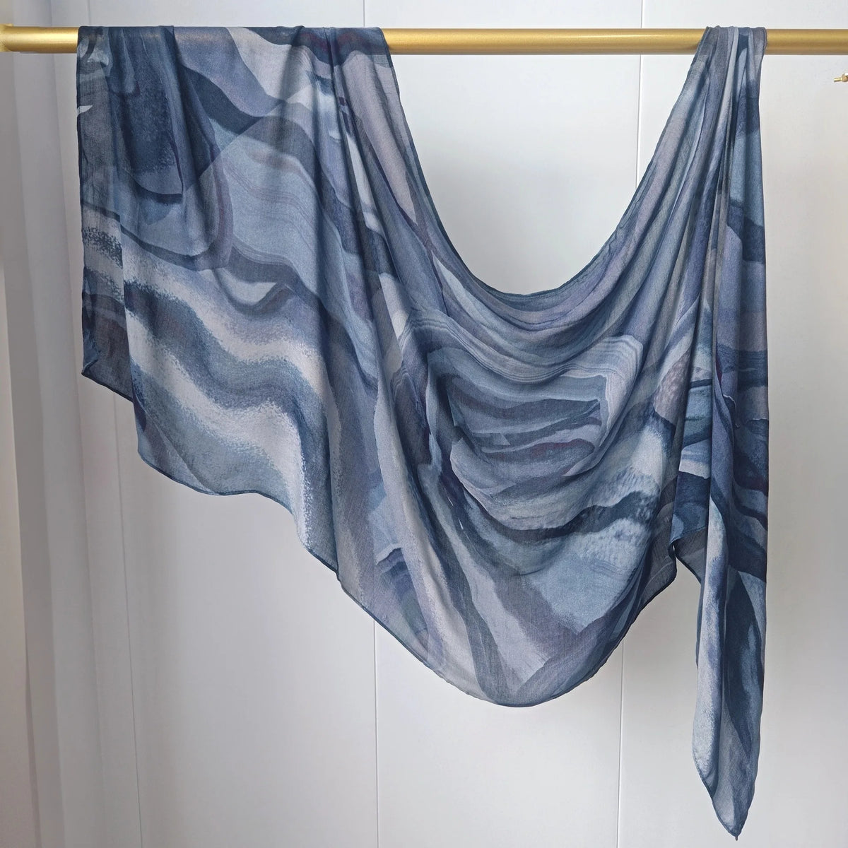 Fließender, durchscheinender blau-grauer Mehrfarben-Hijab-Schal über einem Holzstab drapiert.