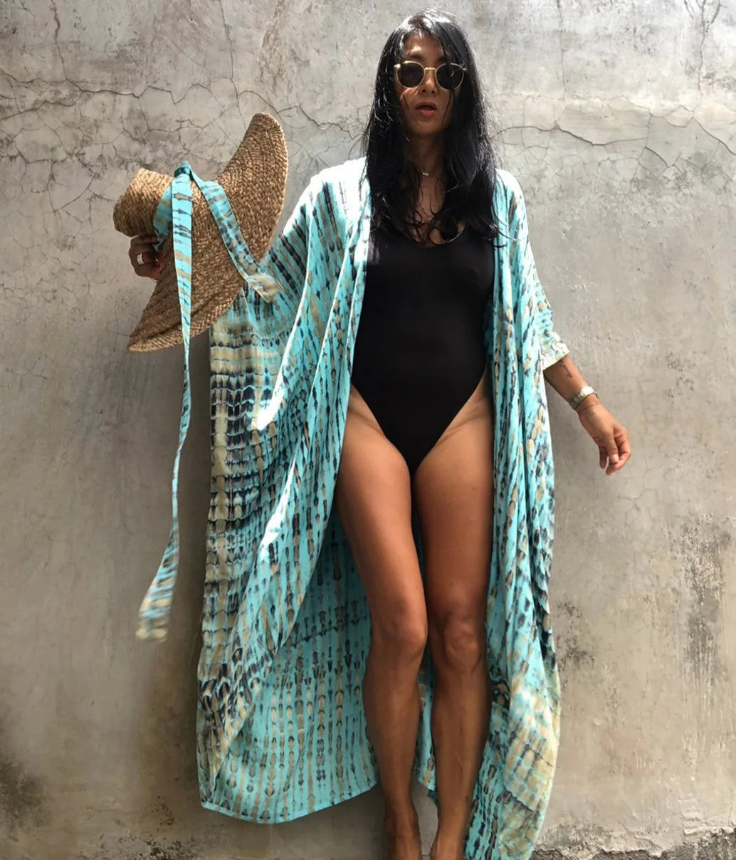 Eine Frau in einem hellblauen gemusterten Kimono-Überkleid über einem schwarzen Badeanzug steht vor einer Betonwand.