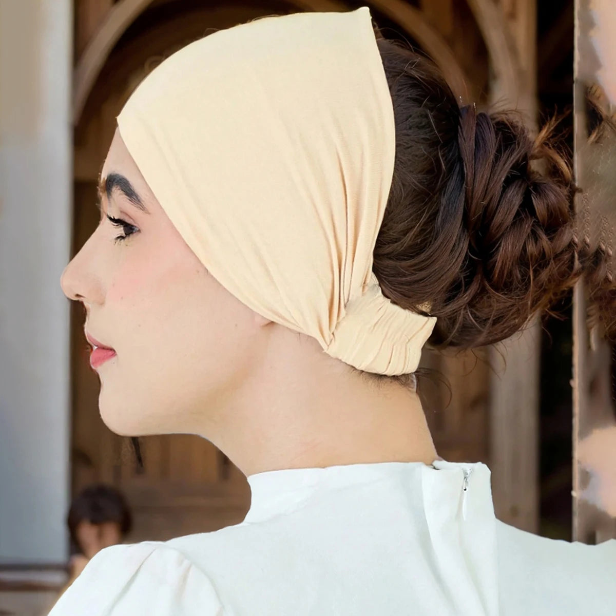 Eine Frau trägt eine beige Premium-Stretch-Baumwoll-Hijab-Underscarf-Kappe mit ihrem Haar zu einem Dutt gestylt.