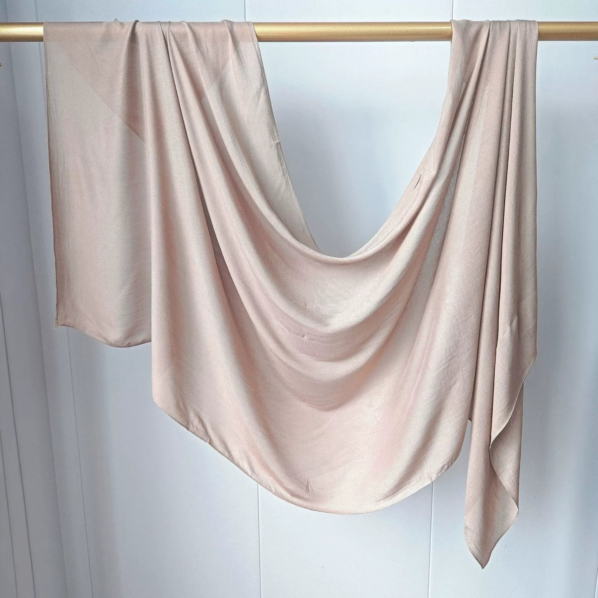 Foulard modal rose pâle uni drapé sur un cintre en bois.
