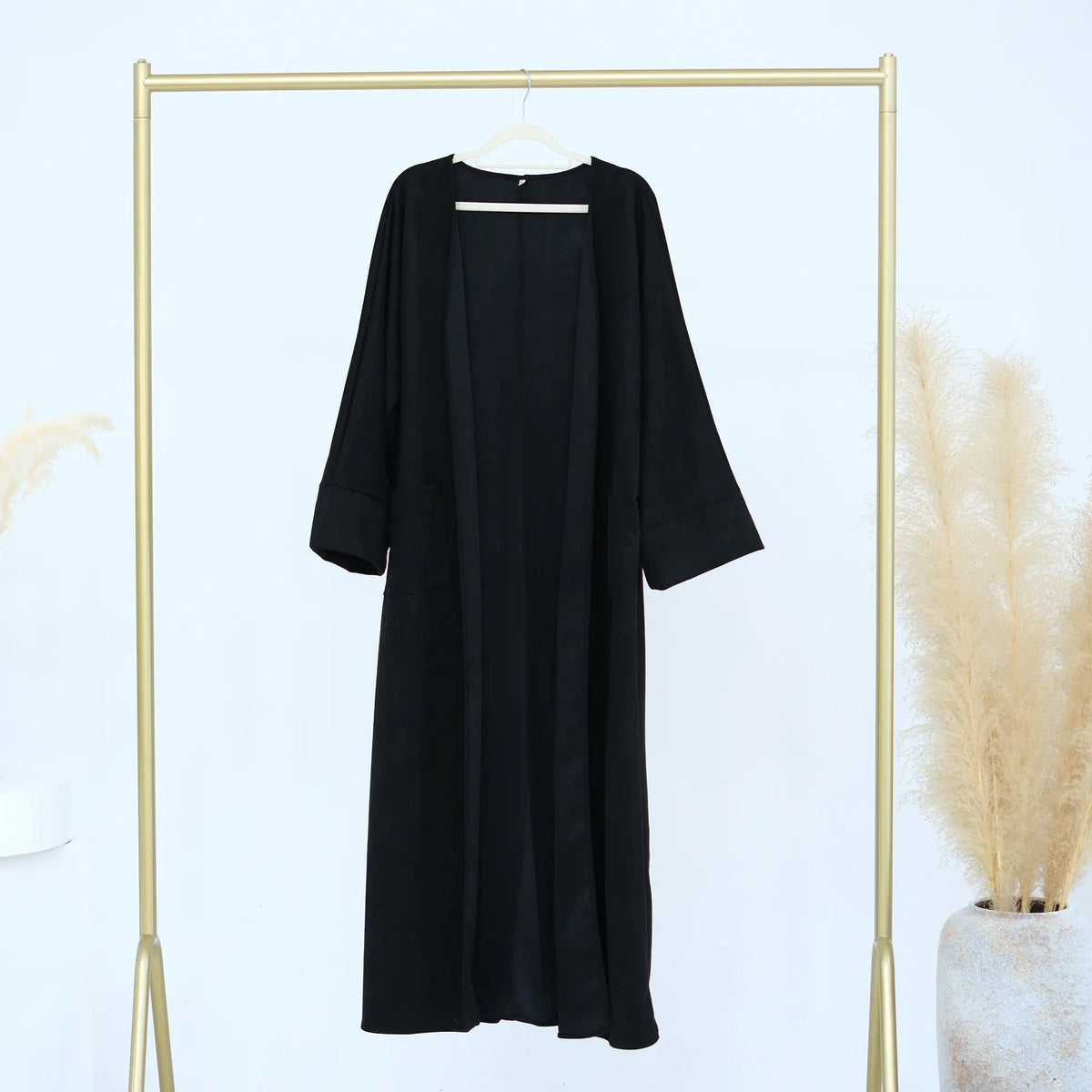 Black elegant women's abaya trench coat displayed on a gold hanger against a white background.
