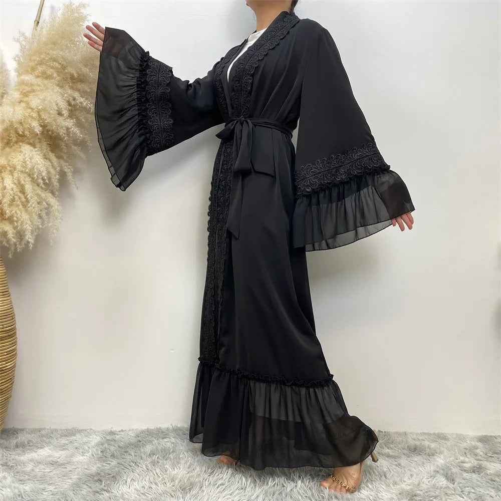 Eine Frau trägt eine elegante, schwarze, bodenlange Abaya mit Spitzenbesatz und weiten Ärmeln.
