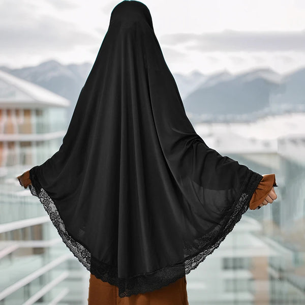 Black full cover instant hijab with lace edge worn by a woman against a city backdrop.