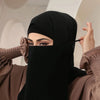 Eine Frau trägt einen schwarzen, atmungsaktiven Netz-Hijab und Halstuch und blickt direkt in die Kamera.
