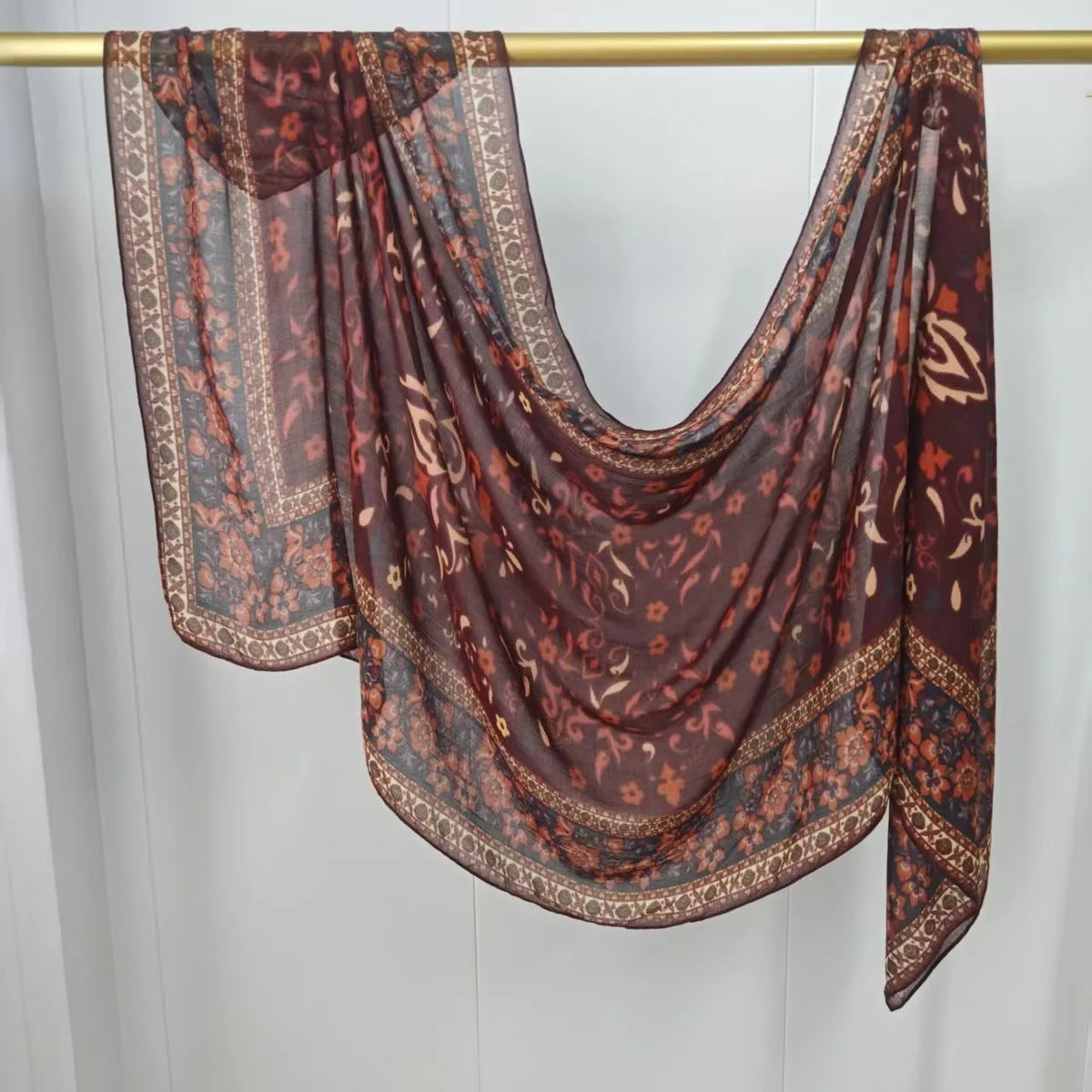 Dunkelbrauner und rostfarbener gemusterter Hijab-Schal über einem goldenen Haken.