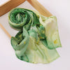 Un foulard voile imprimé vert clair roulé et drapé sur un plateau en bois.
