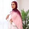 Una mujer vistiendo un pañuelo hijab malva sobre una prenda blanca, de pie en luz brillante.