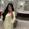 Una mujer vistiendo un elegante caftán de manga larga color crema en un lujoso baño.