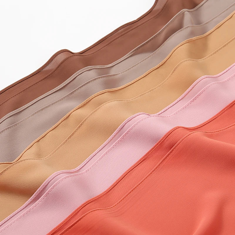Nahaufnahme mehrerer Lagen hochwertiger Chiffon-Hijabs in Beige-, Pfirsich- und Rosa-Tönen.