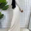 Eine Frau in einem eleganten cremefarbenen Maxi-Abaya-Kleid und einem schwarzen Hijab vor weiß verkleidetem Hintergrund