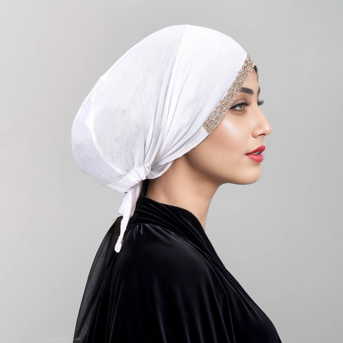 Eine Frau mit weißem Diamant-Hijab und schwarzem Samt-Oberteil, im Profil.