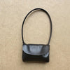 Bolso de cuero negro con correa y cierre de solapa sobre una superficie texturizada marrón claro.