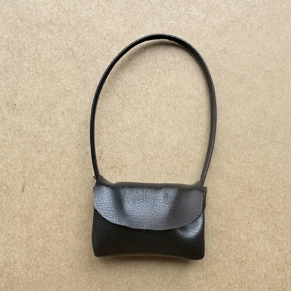 Bolso de cuero negro con correa y cierre de solapa sobre una superficie texturizada marrón claro.