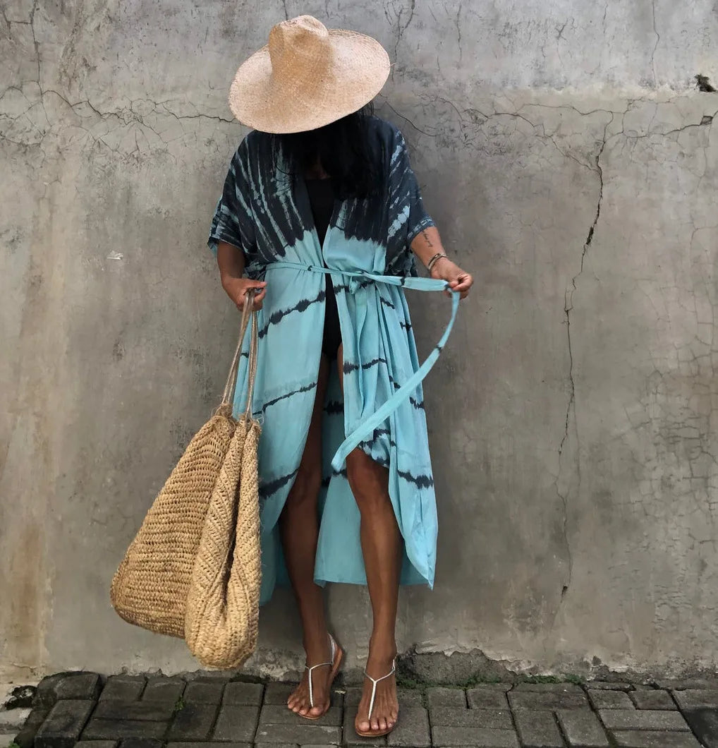 Eine Person in einem hellblauen gemusterten Kimono-Überkleid und einem Strohhut steht vor einer strukturierten grauen Wand.