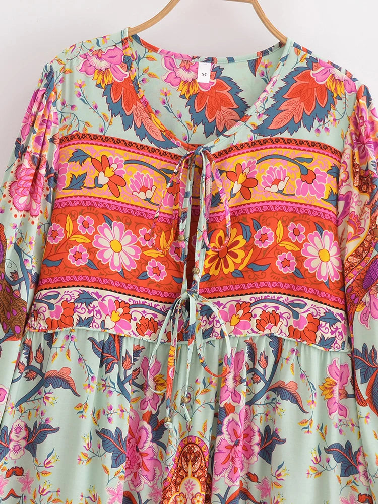 Vestido largo bohemio verde claro con estampados florales vibrantes en rosa, naranja y rojo con detalles de lazos.