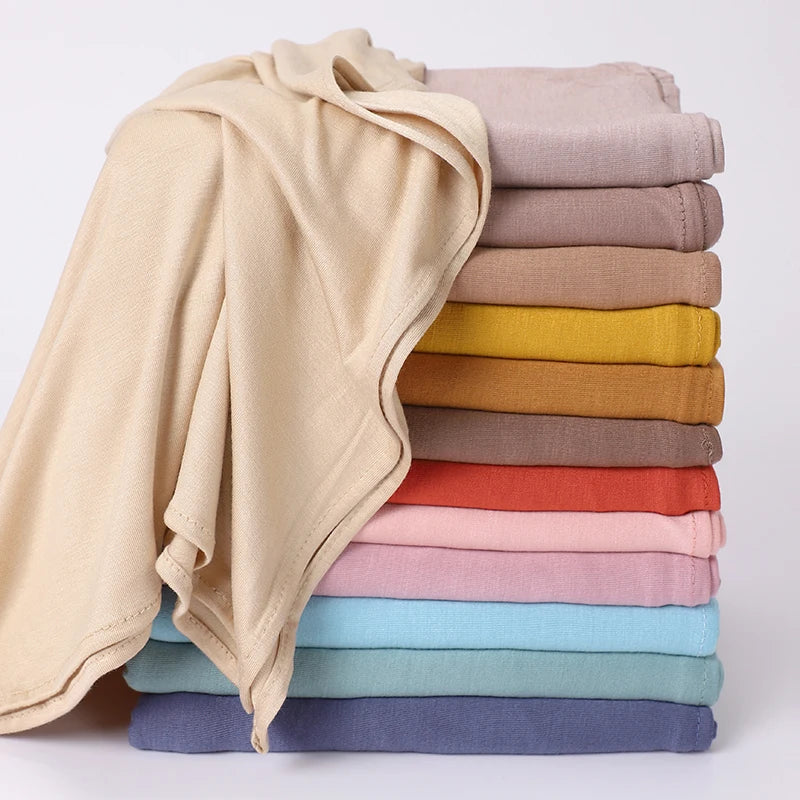 Ein Stapel von Jersey-Hijabs in verschiedenen Beigetönen, Olivgrün, Braun und Pink.