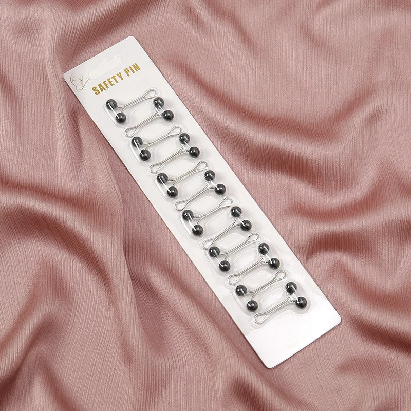 Une épingle de sécurité blanche avec plusieurs épingles décoratives argentées sur un fond de tissu rose.