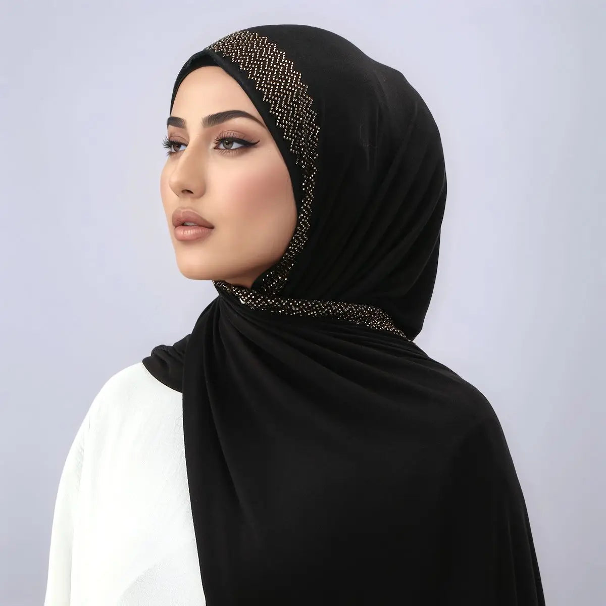Eine Frau trägt ein schwarzes Hijab mit goldenen Pailletten und einem weißen Kleidungsstück.