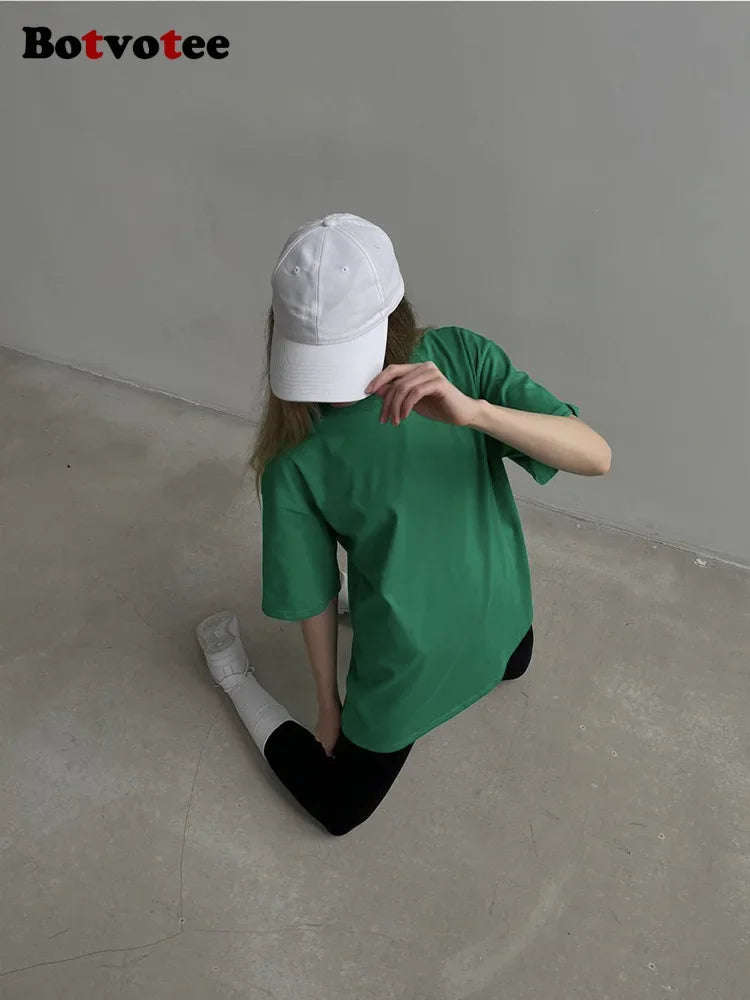 Una persona vistiendo una camiseta básica verde de algodón oversize y una gorra blanca, vista desde atrás.