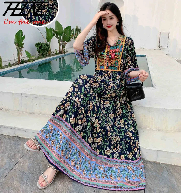Eine Frau modelliert ein dunkelblaues, bohémisches besticktes Maxi-Kleid mit Blumenmustern und rosa Rand.