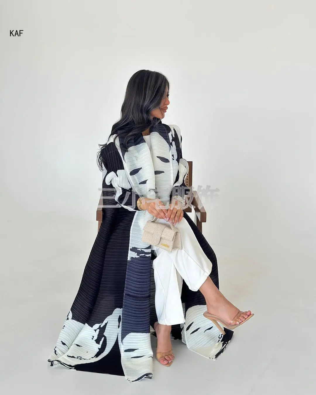 Une femme modélise une veste coupe-vent plissée imprimée noir et blanc avec un pantalon blanc.