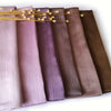 Eine Reihe von gerüschten Satin-Chiffon-Hijabs in verschiedenen Violett- und Brauntönen mit goldenen Akzenten.