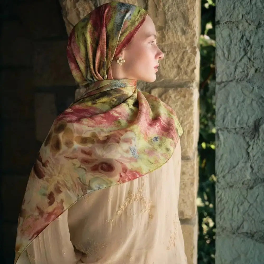 Eine Frau trägt einen eleganten bedruckten Seideschal-Hijab in sanften rosa und grünen Tönen, im Profil dargestellt.