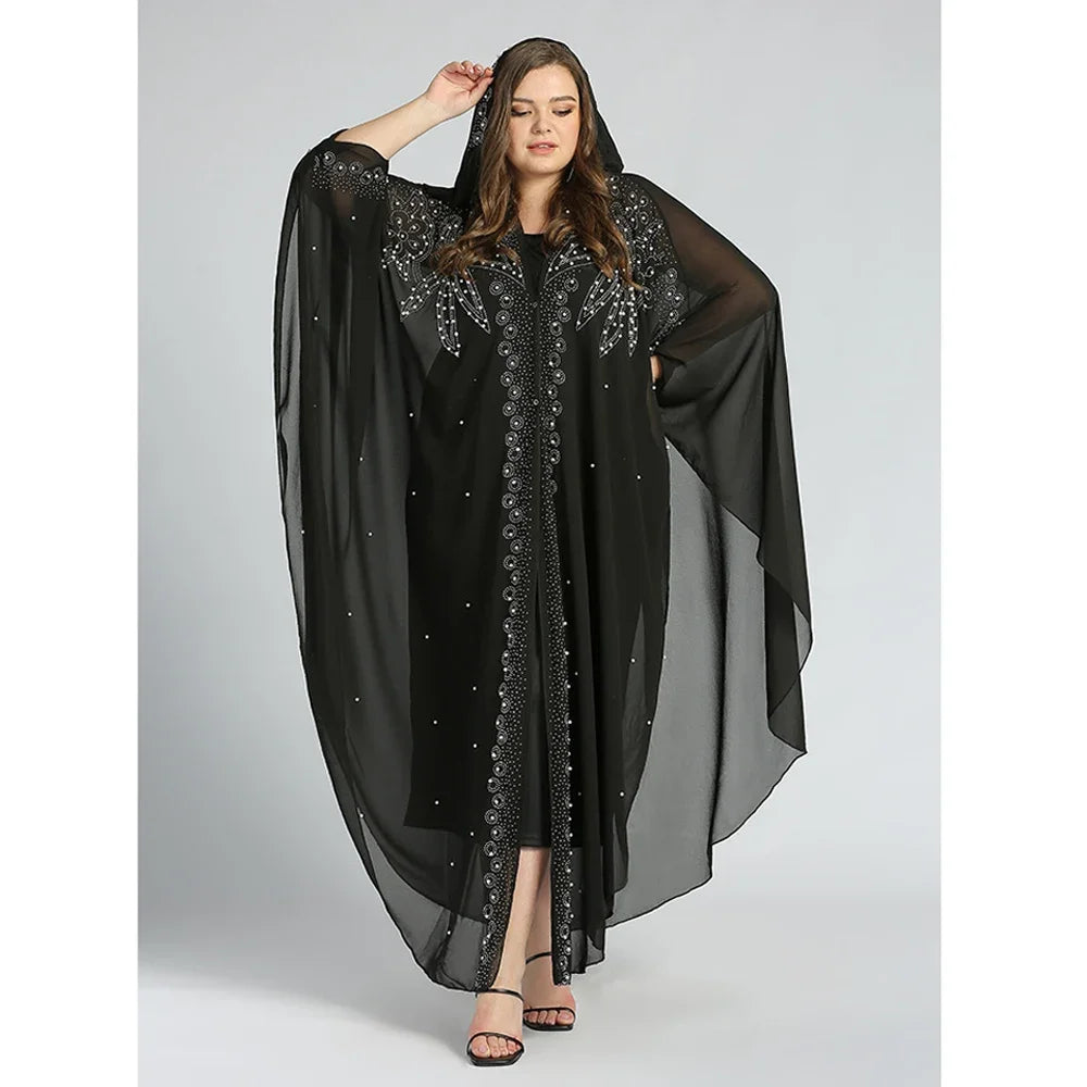 Una mujer vistiendo un abaya largo y fluido negro con mangas de murciélago y superposición transparente.