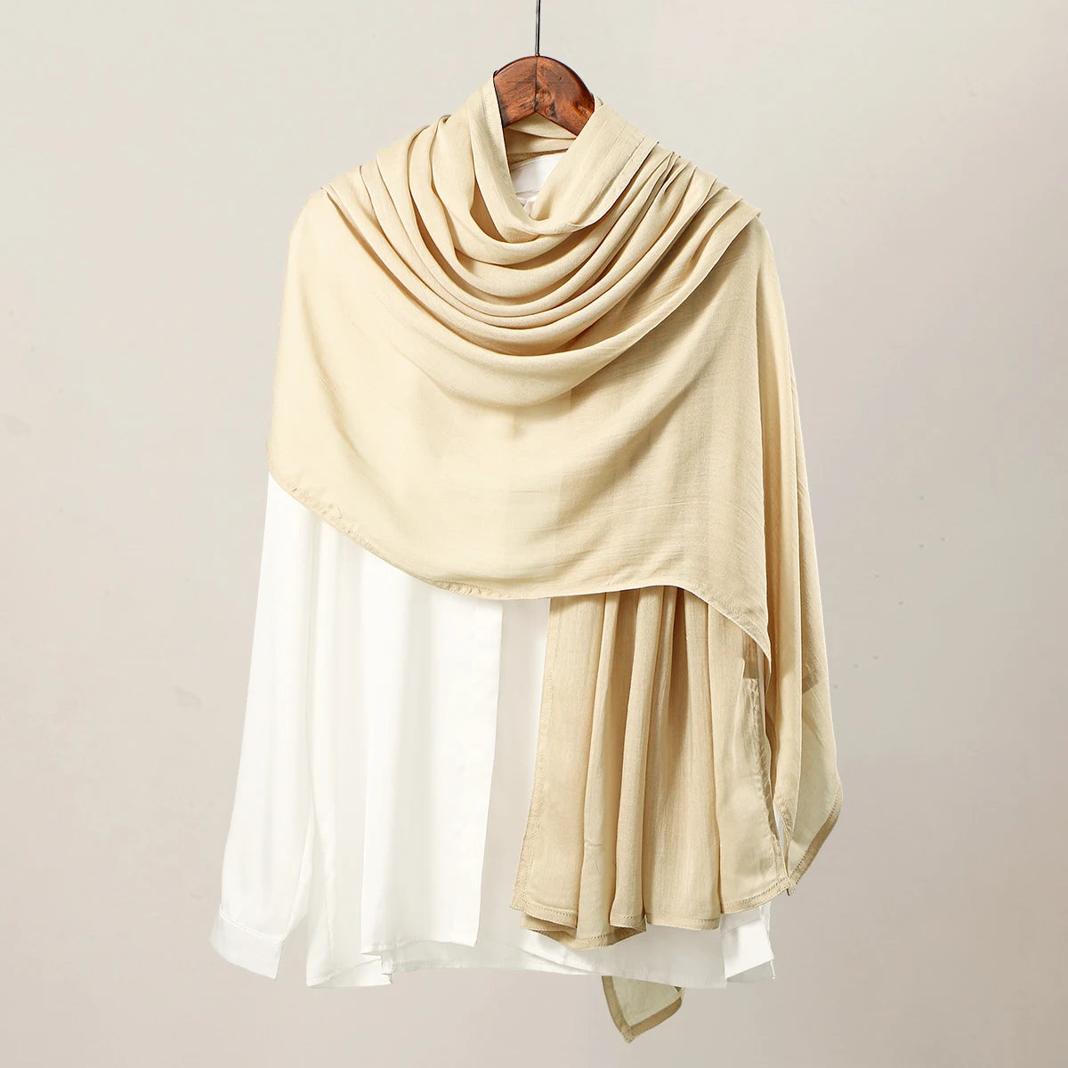 Pañuelo de hijab de modal rayón beige drapeado sobre una blusa blanca de manga larga.