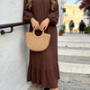 Une femme portant une longue robe bohème marron à volants et tenant un sac en paille tissé à l'extérieur.