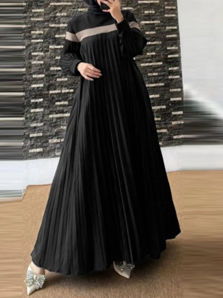 Une femme portant une longue caftan noire plissée avec une bordure beige, debout sur un fond texturé sombre.