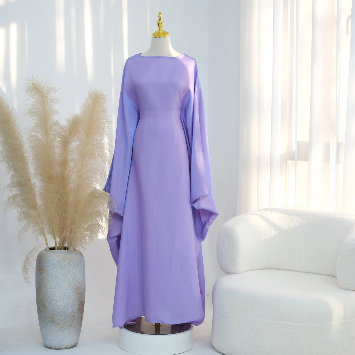 Lila Kaftankleid mit Schmetterlingsärmeln auf einem Mannequin neben getrocknetem Pampasgras.