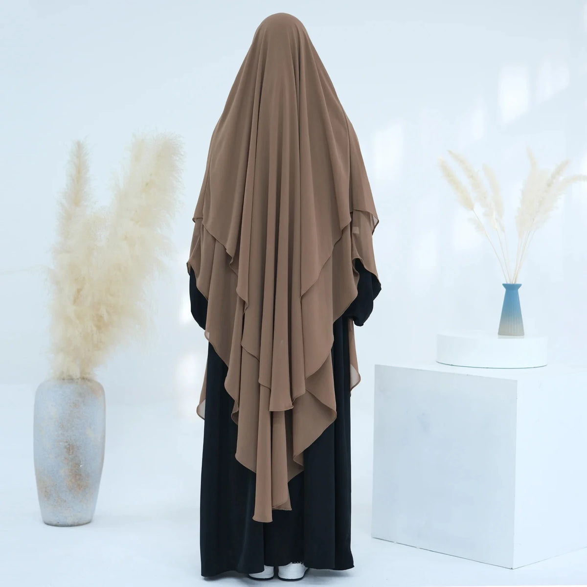 Eine Frau trägt einen beige-beigen, zweilagigen Chiffon-Niqab und schwarze Kleidung in einer hellen, minimalistischen Umgebun