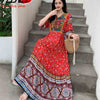 Eine Frau in einem rot-blauen, bohemieninspirierten bestickten Maxi-Kleid steht auf Außentreppen.