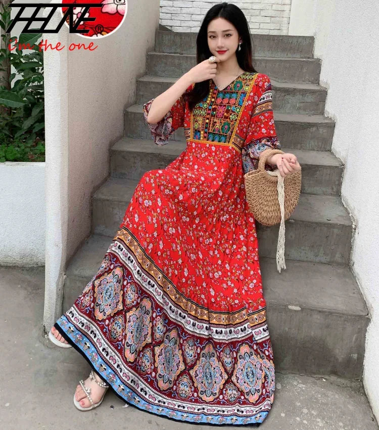 Eine Frau in einem rot-blauen, bohemieninspirierten bestickten Maxi-Kleid steht auf Außentreppen.