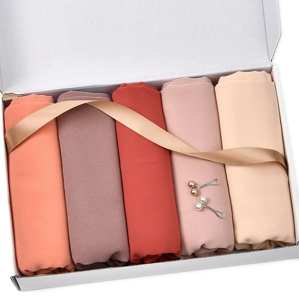 A box containing five rolled chiffon hijab scarves in shades of peach, coral, and nude.