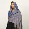 Una mujer modela un pañuelo pashmina de lujo con estampado azul y dorado sobre su cabeza y hombros.