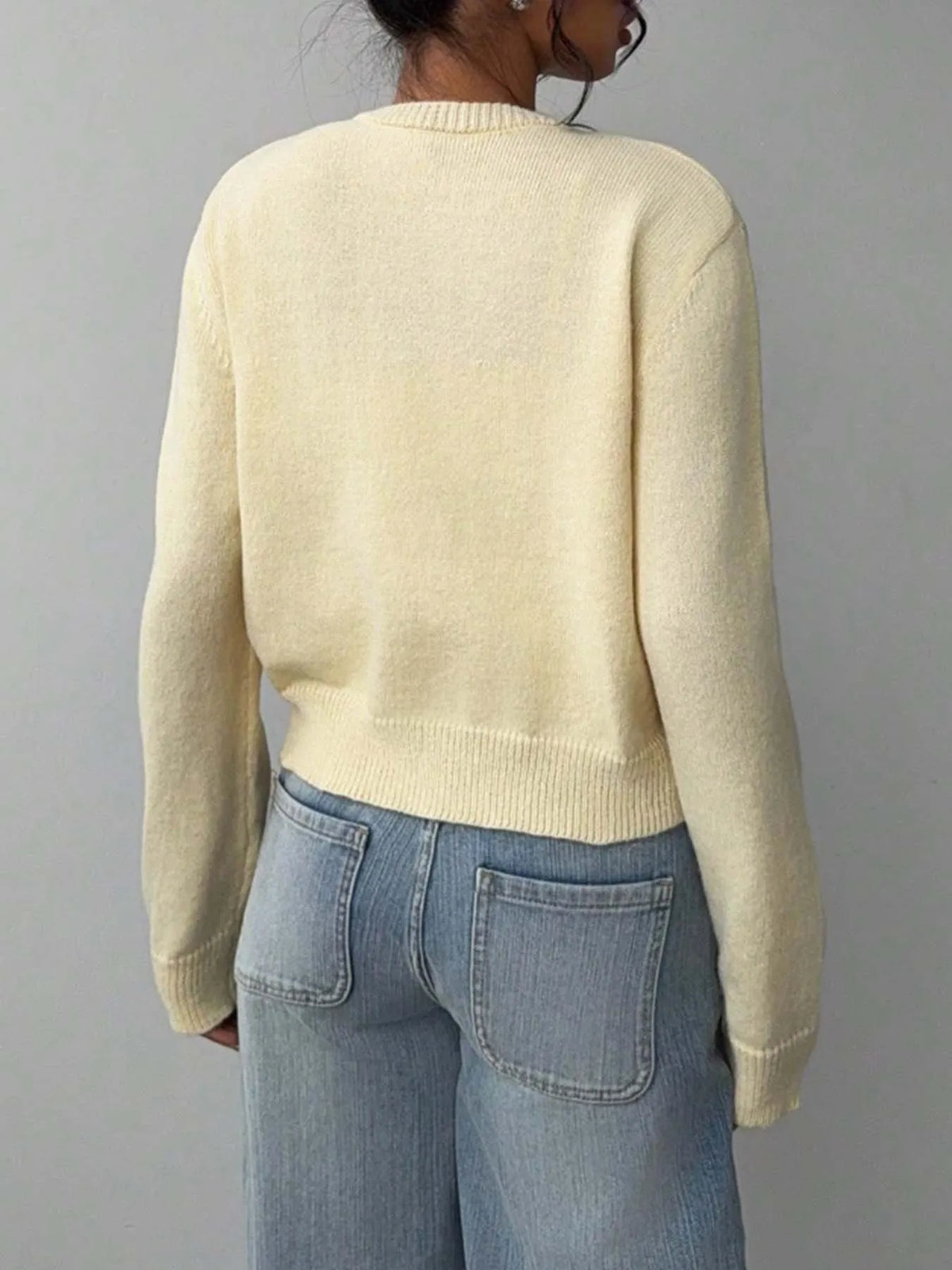 Une femme vue de dos portant un pull tricoté crème et un jean bleu.