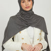 Eine Frau trägt einen einfarbigen grauen Jersey-Hijab und eine weiße strukturierte Jacke.